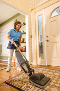 A Maid To Please employee vacuums a rug by the front door of a home.