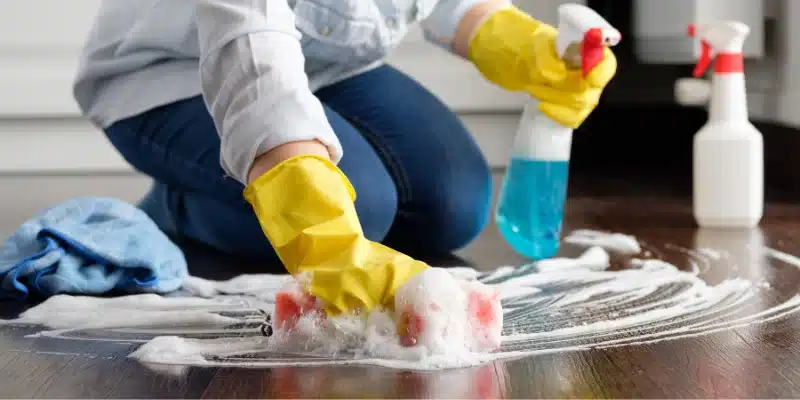 A cleaner scrubs a floor with soap and a sponge.